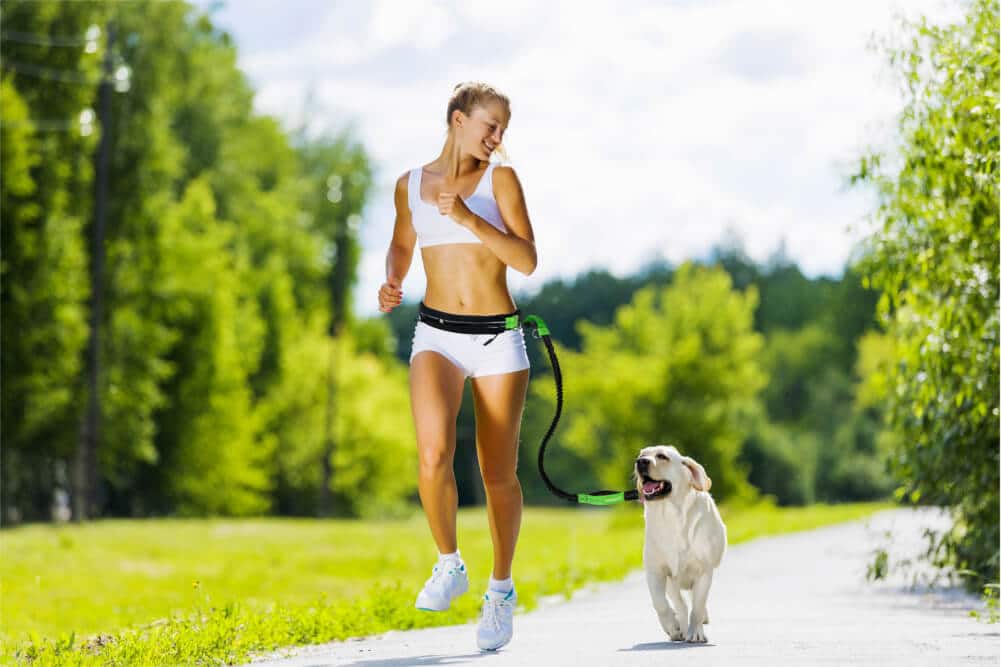 Eine Frau joggt mit ihrem Hund und einer Joggingleine im Park